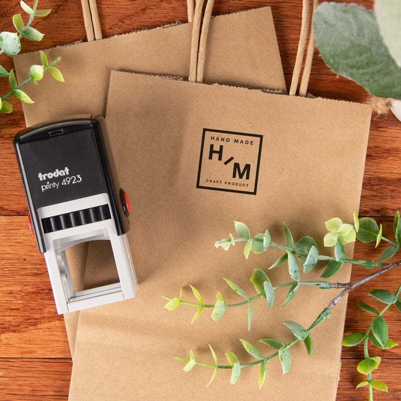 Trodat Printy 4923 logo stamp shown beside a kraft paper bag with a handmade logo imprint