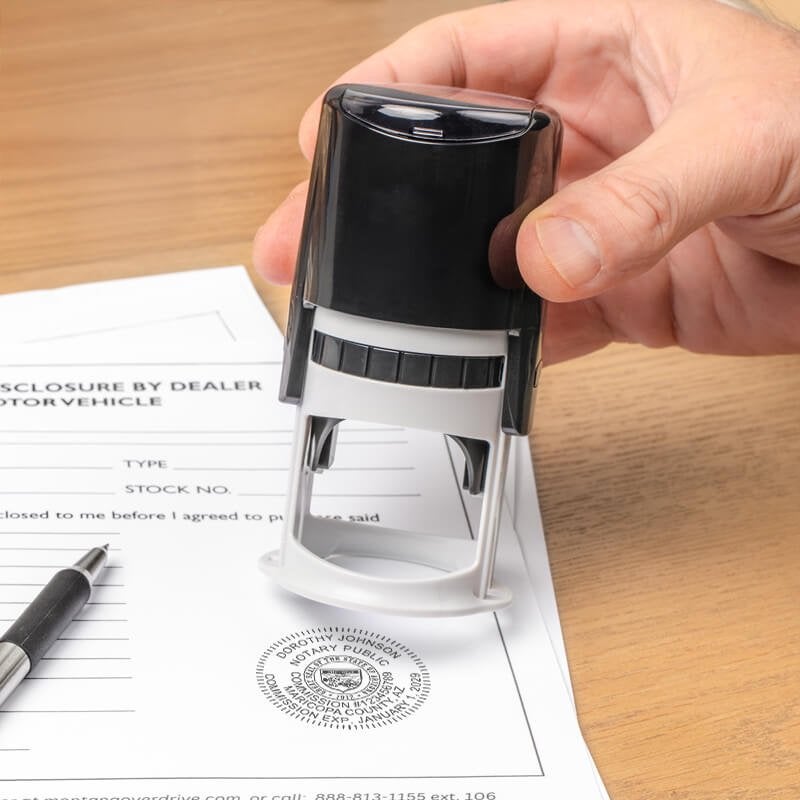 Hand stamping Arizona notary seal on official document with pen on wooden desk.