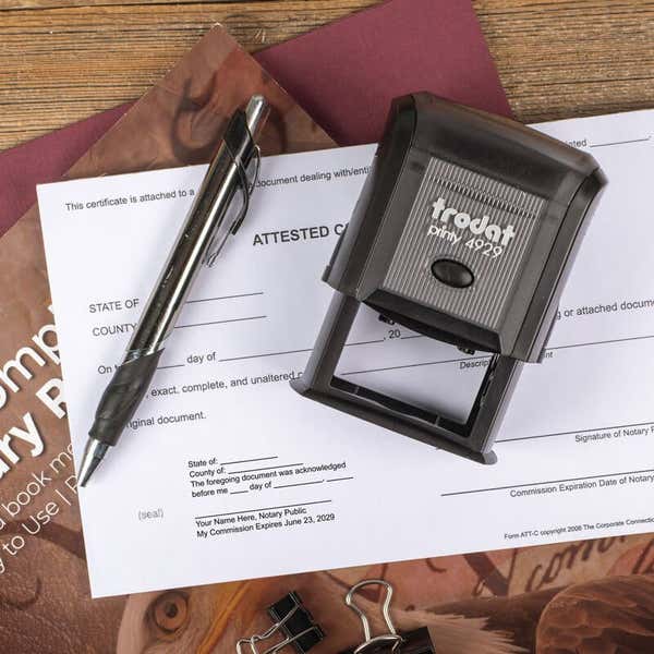 Trodat Printy 4929 stamp placed next to a notary form with a black stamped impression and office supplies