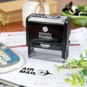 Simply Stamps Trodat Printy 4915 custom stamp shown stamping 'AIR MAIL' with airplane graphic on mailing documents, ideal for shipping, packaging, or business correspondence.