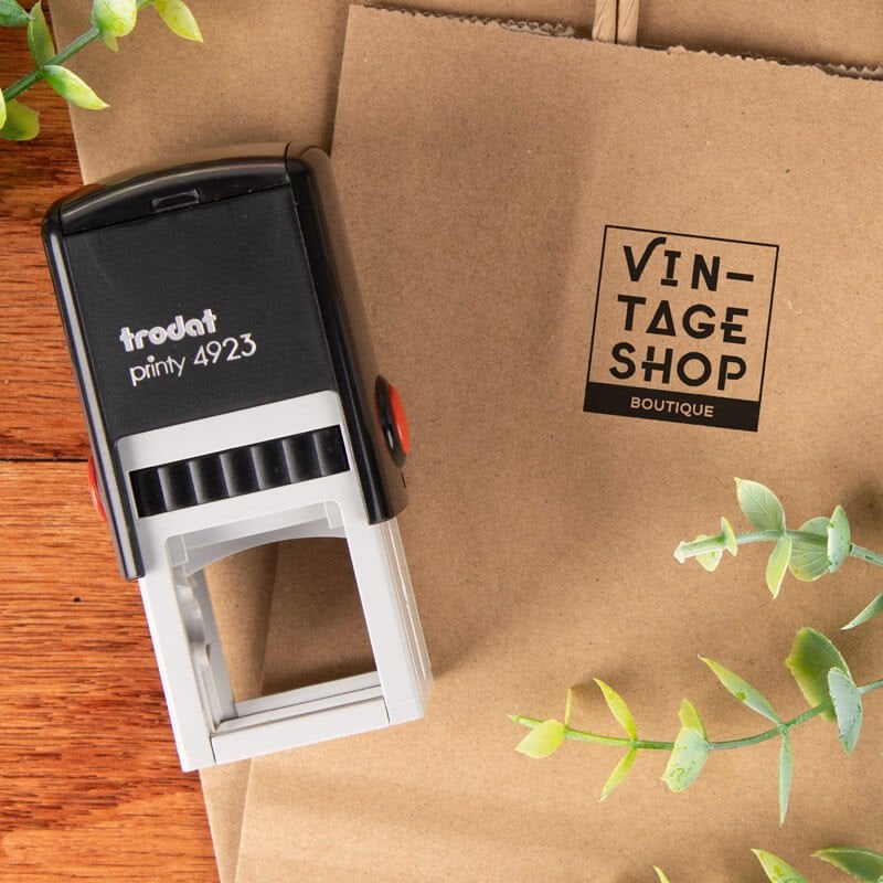 Trodat Printy 4923 custom stamp shown next to a kraft paper bag stamped with a boutique logo