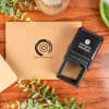 Self-inking stamp next to a kraft envelope stamped with an Instagram handle and logo