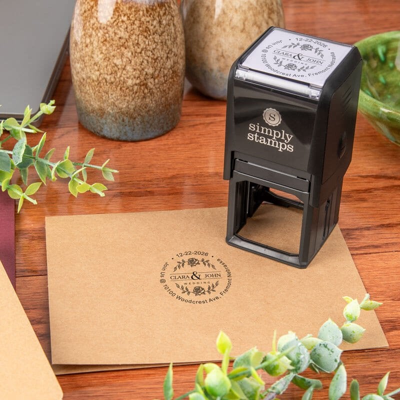 Logo stamp design being used for custom wedding stamp impression reading “Clara & John” with floral design and address details, shown on envelope with Simply Stamps self-inking stamp