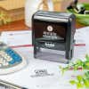 Simply Stamps self-inking stamp resting on a document that has been stamped with a business logo and informational text