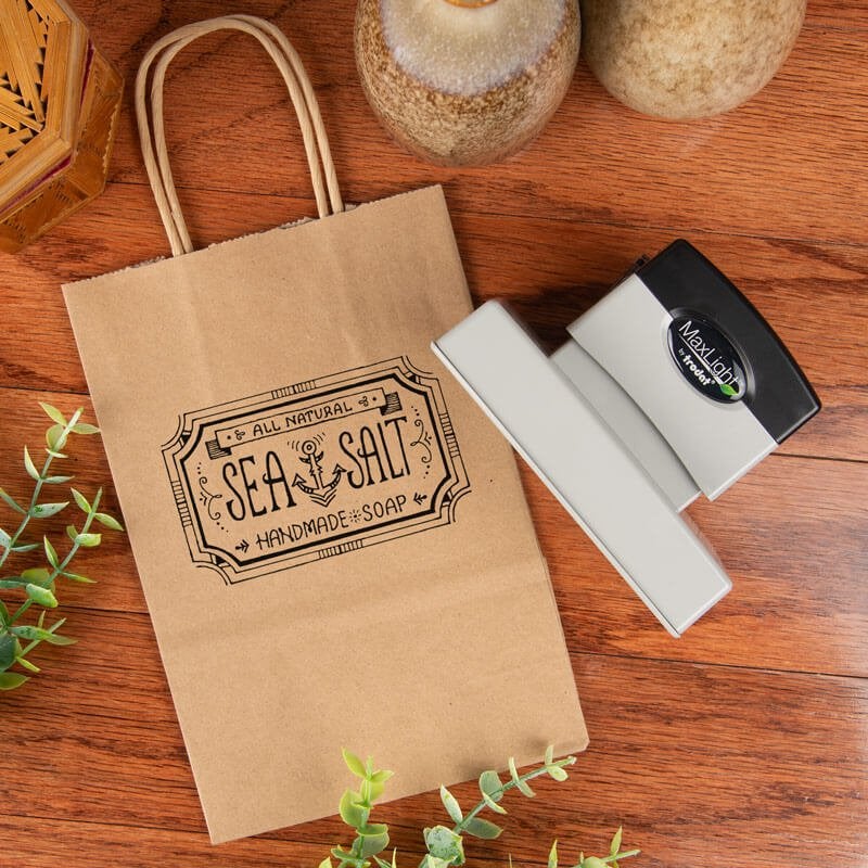 MaxLight XL 275 pre-inked logo stamp used to brand kraft paper packaging for handmade soap, showcasing high-detail custom stamping for small business products.