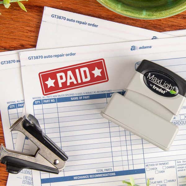 MaxLight by Trodat pre-inked stamp laying on an auto repair order form with a red PAID stamp impression