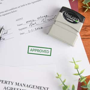 MaxLight pre-inked stamp laying on paperwork sample with a green "APPROVED" stamp impression
