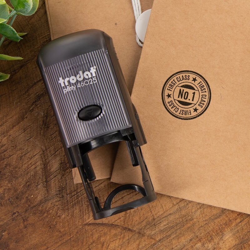 Trodat Printy 46025 self-inking stamp placed beside a kraft paper package featuring a stamped design