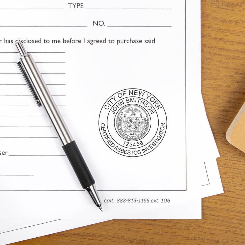 The New York Asbestos Investigator stamp on a document next to a pen