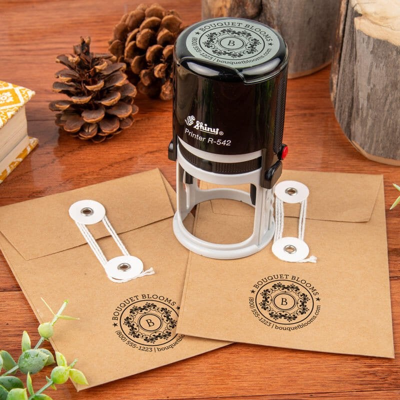 Branded Shiny R-542 round stamp resting on kraft clasp envelopes stamped with a boutique-style floral logo