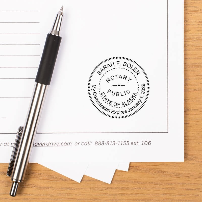 Alaska notary stamp impression on white paper with a pen.