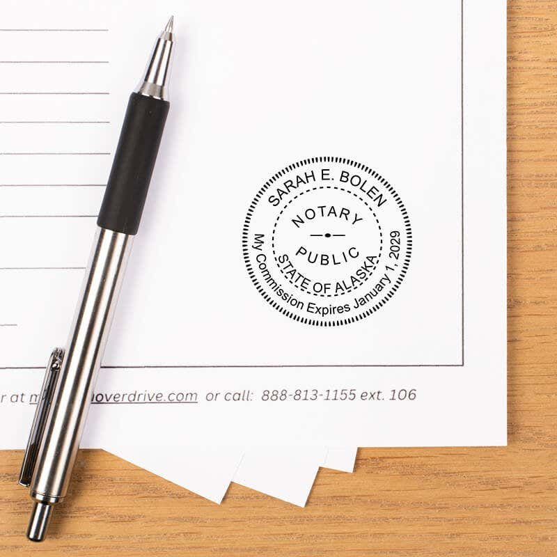 Alaska notary stamp impression on white paper with a pen.