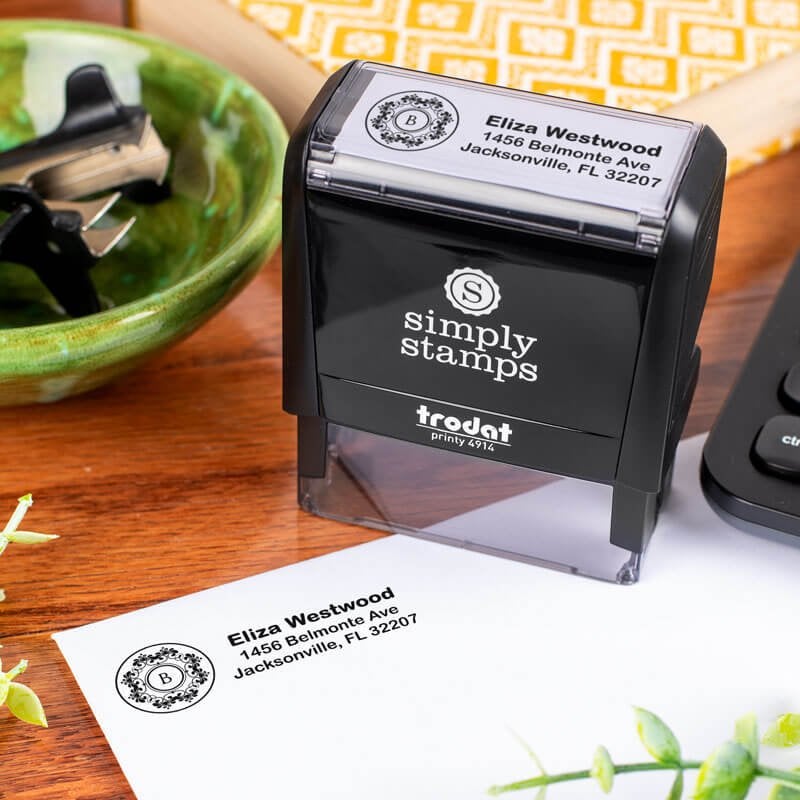 Trodat Printy 4914 self-inking address stamp customized with name and floral monogram, shown stamping a return address on an envelope