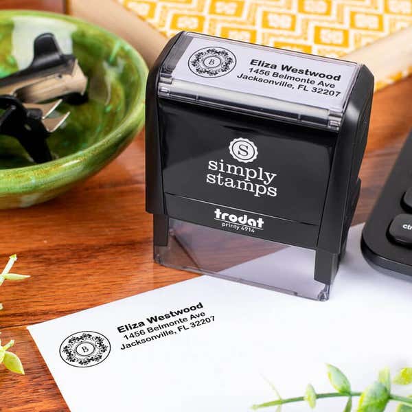 Trodat Printy 4914 self-inking address stamp customized with name and floral monogram, shown stamping a return address on an envelope