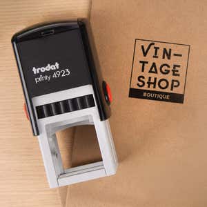 Small Custom Logo Stamp, 1"x1" resting beside a freshly stamped custom logo impression