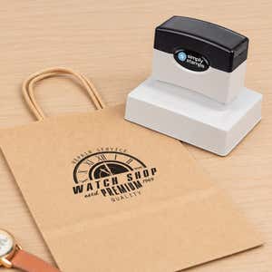 Medium Custom Logo Stamp, 2-3/8" x 3-1/4" resting beside a freshly stamped custom logo impression