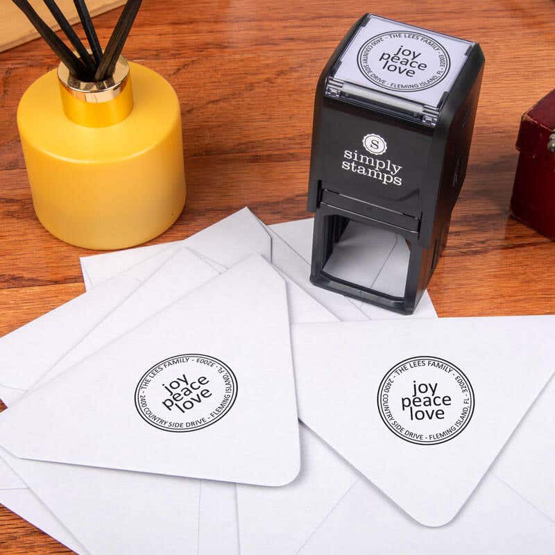 Joy Peace Love Round Address Stamp design impression on two envelopes next to self inking stamp body