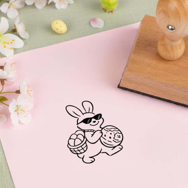Easter bunny basket stamped in black on pink cardstock beside white blossoms, a speckled candy egg and the wooden stamp