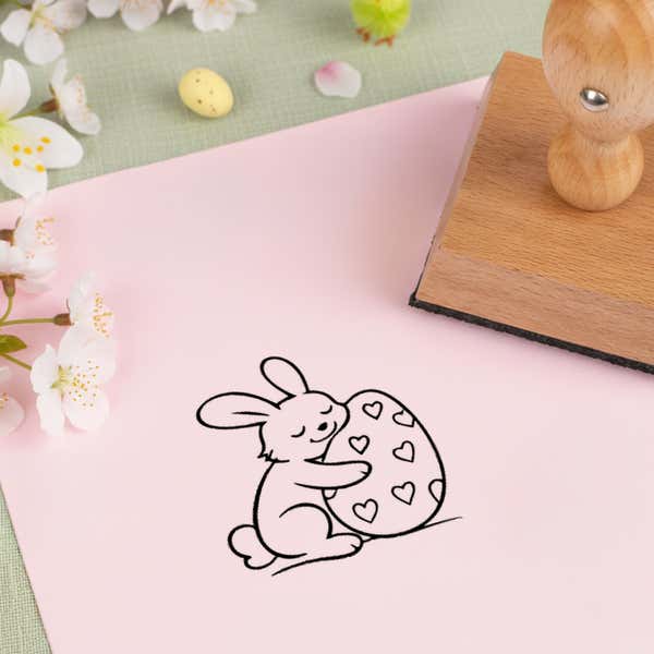 hoppy bunny egg stamped in black on pink cardstock beside white blossoms, a speckled candy egg and the wooden stamp
