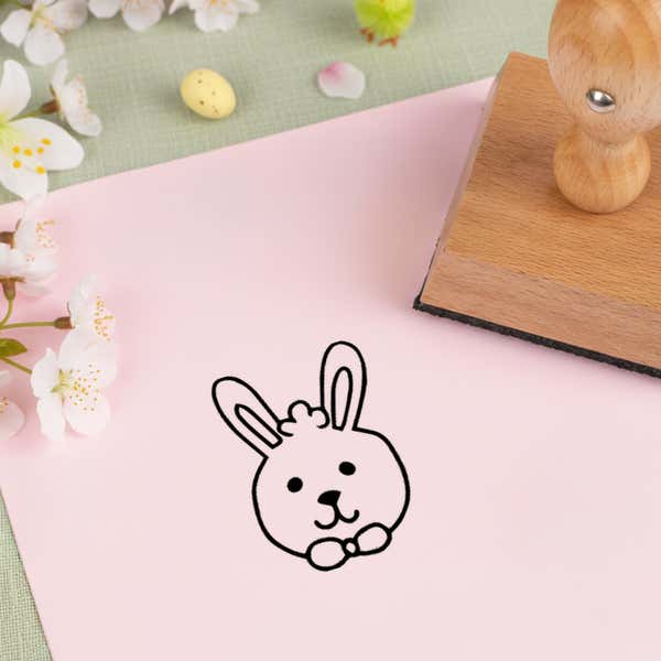 cute bunny face stamped in black on pink cardstock beside white blossoms, a speckled candy egg and the wooden stamp