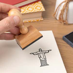 Hand pressing the Christ the Redeemer Craft Stamp onto cardstock beside a black ink pad