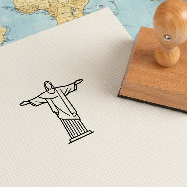 Christ the Redeemer stamped in black on cream graph paper laid over a world map, with the wooden stamp nearby