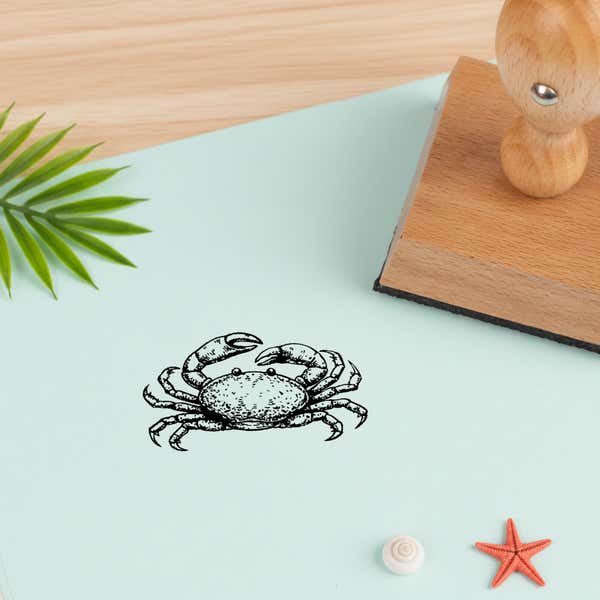 ocean crab stamped in black on mint green cardstock beside a palm leaf, a tiny white shell and an orange starfish