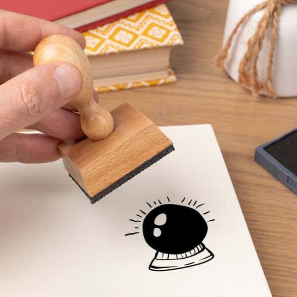 Hand pressing the Mystic Crystal Ball Craft Stamp onto cardstock beside a black ink pad