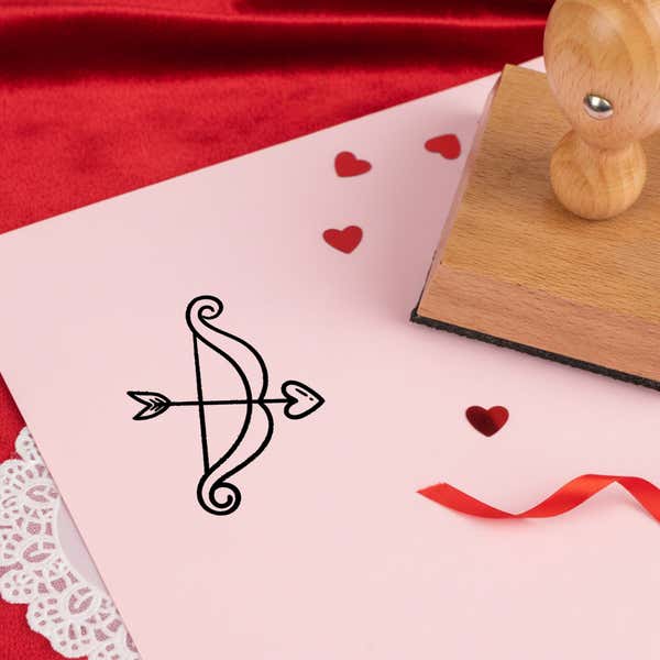 playful cupid bow stamped in black on pink cardstock with red heart confetti, ribbon, a lace doily and the stamp