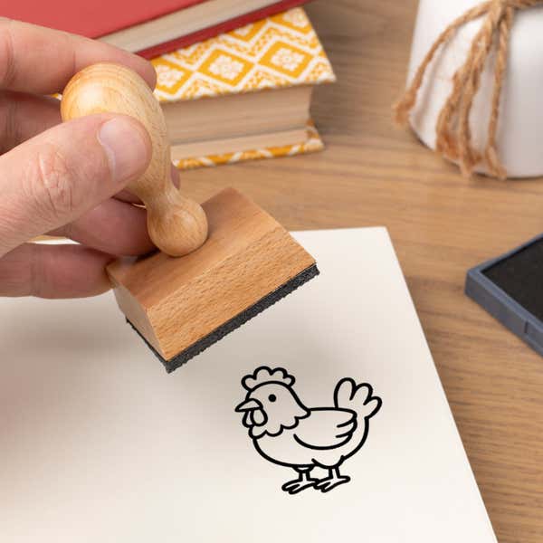 Hand pressing the Cute Chicken Craft Stamp onto cardstock beside a black ink pad