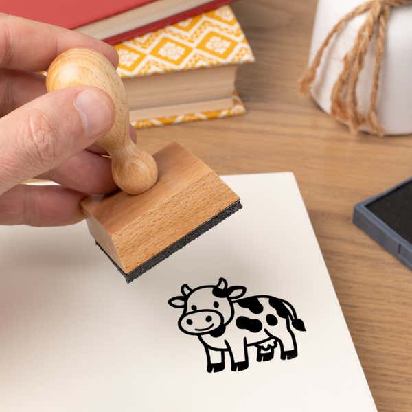 Hand pressing the Cute Cow Craft Stamp onto cardstock beside a black ink pad