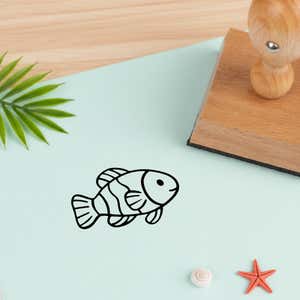 cute striped fish stamped in black on mint cardstock near the wooden stamp, a palm leaf, a white shell and a tiny starfish