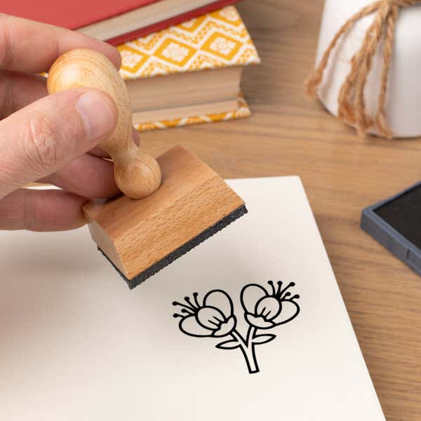 Hand pressing the Twin Blossom Branch Craft Stamp onto cardstock beside a black ink pad