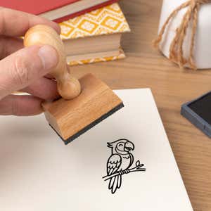 Hand pressing the Cute Parrot Craft Stamp onto cardstock beside a black ink pad