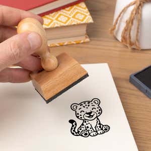 Hand pressing the Cute Spotted Cat Craft Stamp onto cardstock beside a black ink pad