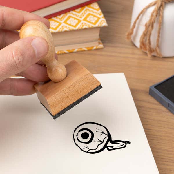 Hand pressing the Watchful Eyeball Craft Stamp onto cardstock beside a black ink pad