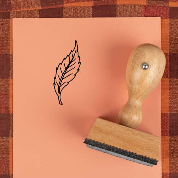 Curved serrated leaf stamped in black on peach cardstock on a plaid autumn cloth