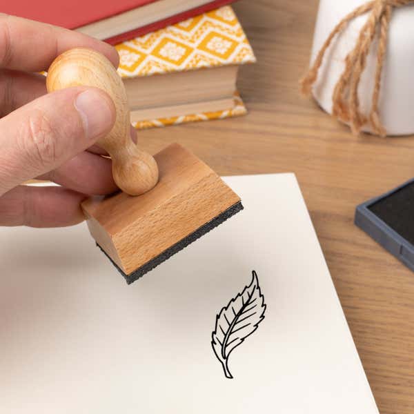 Hand pressing the Curved Serrated Leaf Craft Stamp onto cardstock beside a black ink pad