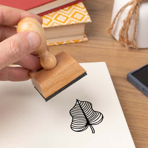 Hand pressing the Striped Vein Leaf Craft Stamp onto cardstock beside a black ink pad