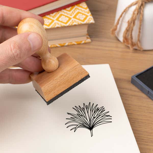 Hand pressing the Fanned Grass Spray Craft Stamp onto cardstock beside a black ink pad