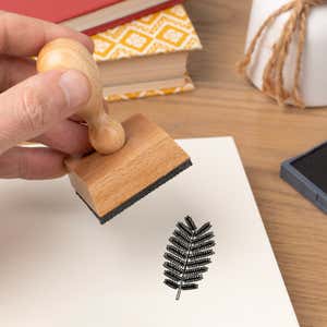 Hand pressing the Fern Frond Craft Stamp onto cardstock beside a black ink pad