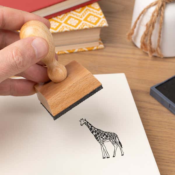 Hand pressing the Safari Giraffe Craft Stamp onto cardstock beside a black ink pad