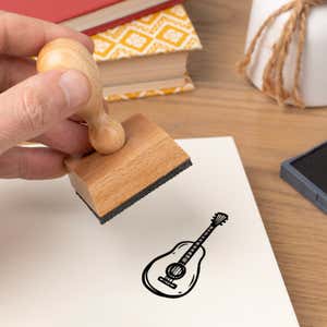 Hand pressing the Guitar Craft Stamp onto cardstock beside a black ink pad