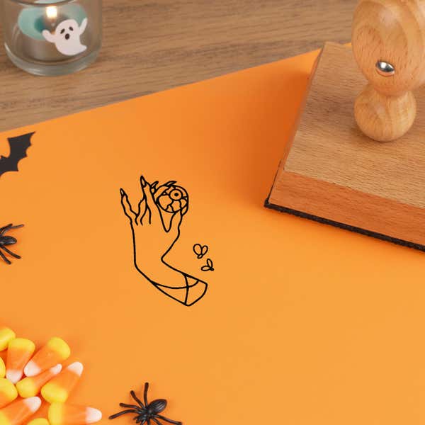 eerie hand eye stamped in black on orange cardstock among candy corn, plastic spiders and a ghost tea light