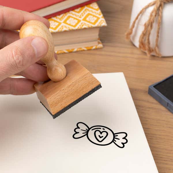 Hand pressing the Sugary Heart Candy Craft Stamp onto cardstock beside a black ink pad