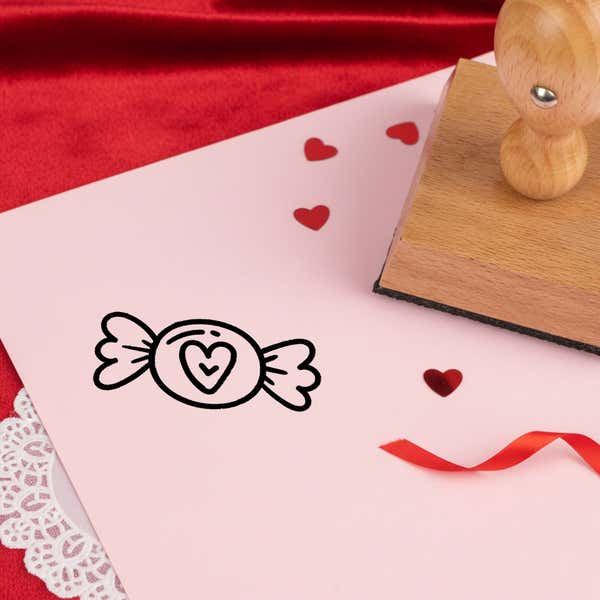 sugary heart candy stamped in black on pink cardstock with red heart confetti, ribbon, a lace doily and the stamp
