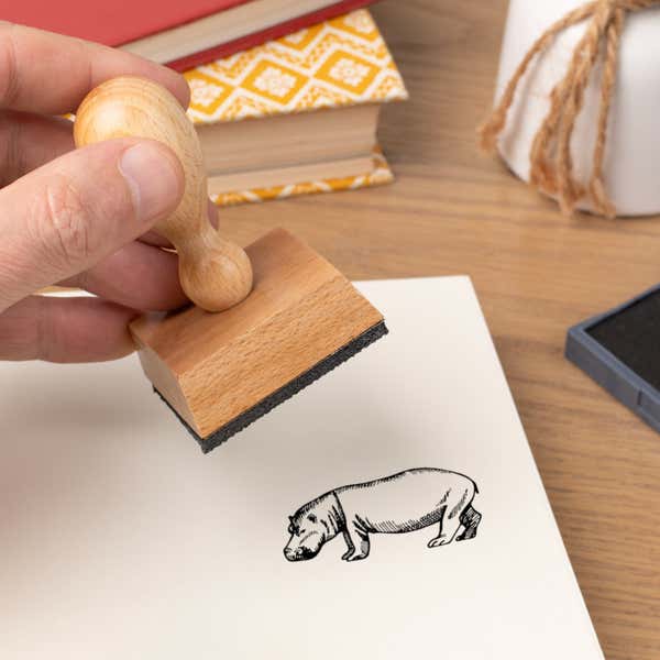 Hand pressing the Safari Hippo Craft Stamp onto cardstock beside a black ink pad