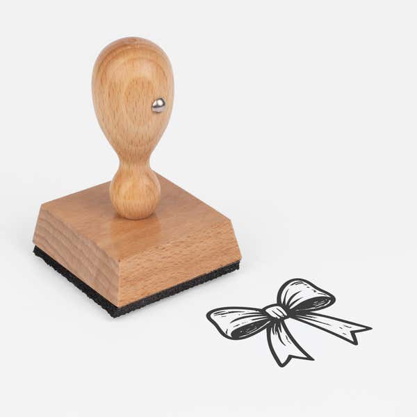 Festive Gift Bow Craft Stamp at an angle, showing the wooden handle, square block and stamped festive gift bow