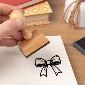 Hand pressing the Festive Gift Bow Craft Stamp onto cardstock beside a black ink pad