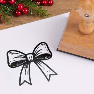Festive gift bow stamped in black on white cardstock styled with red berries and pine greenery